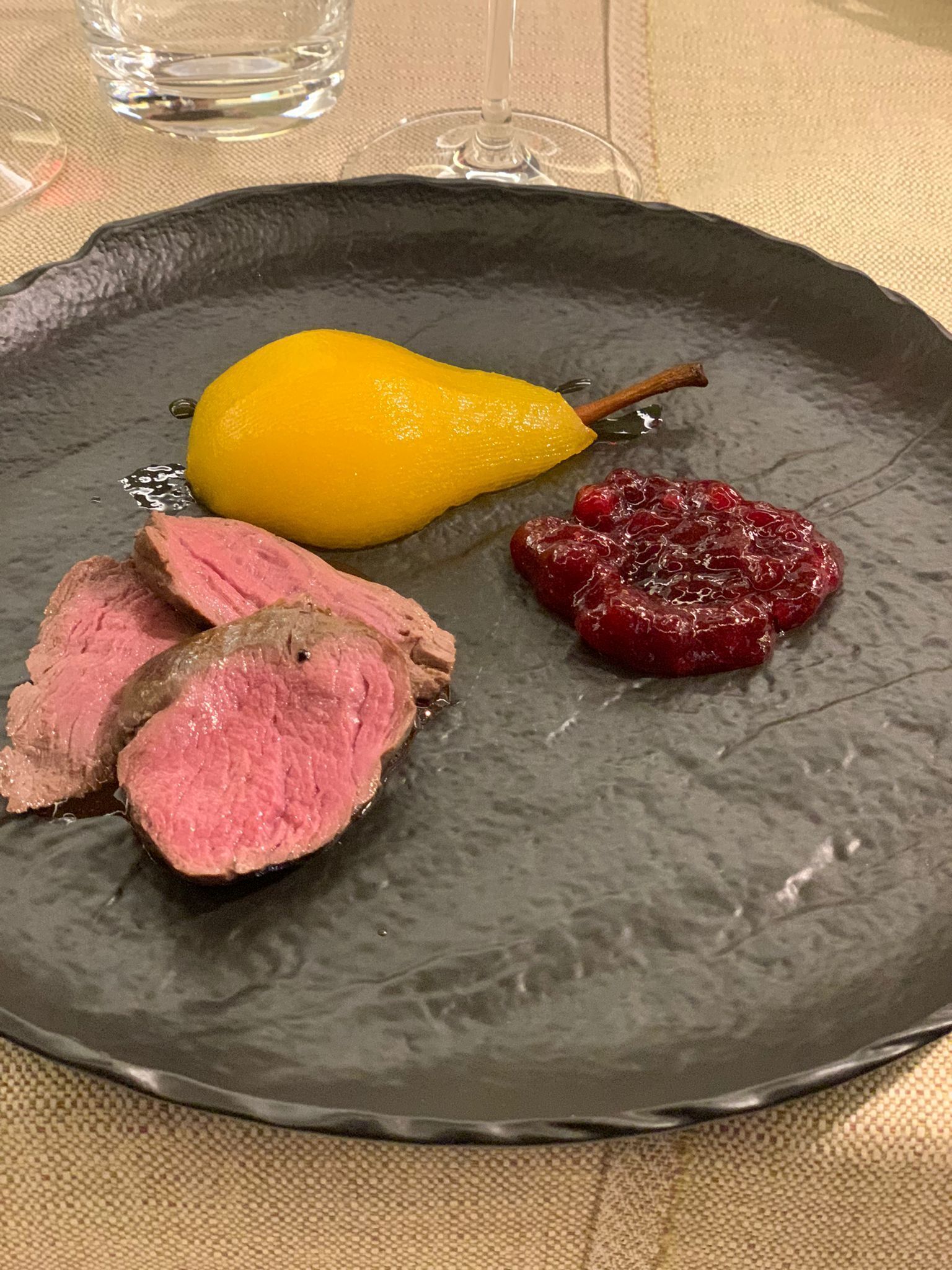 Une assiette avec des tranches de viande, une poire et une compote de fruits rouges.