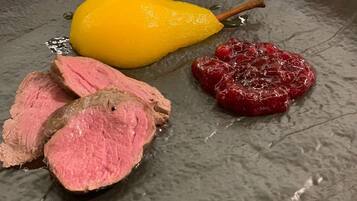 Une assiette avec des tranches de viande, une poire et une compote de fruits rouges.