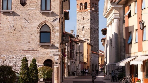 A narrow street with historic buildings, including a prominent tower and a building with a large arched window. - LOcanda ai Provveditori (Marano Lagunare)