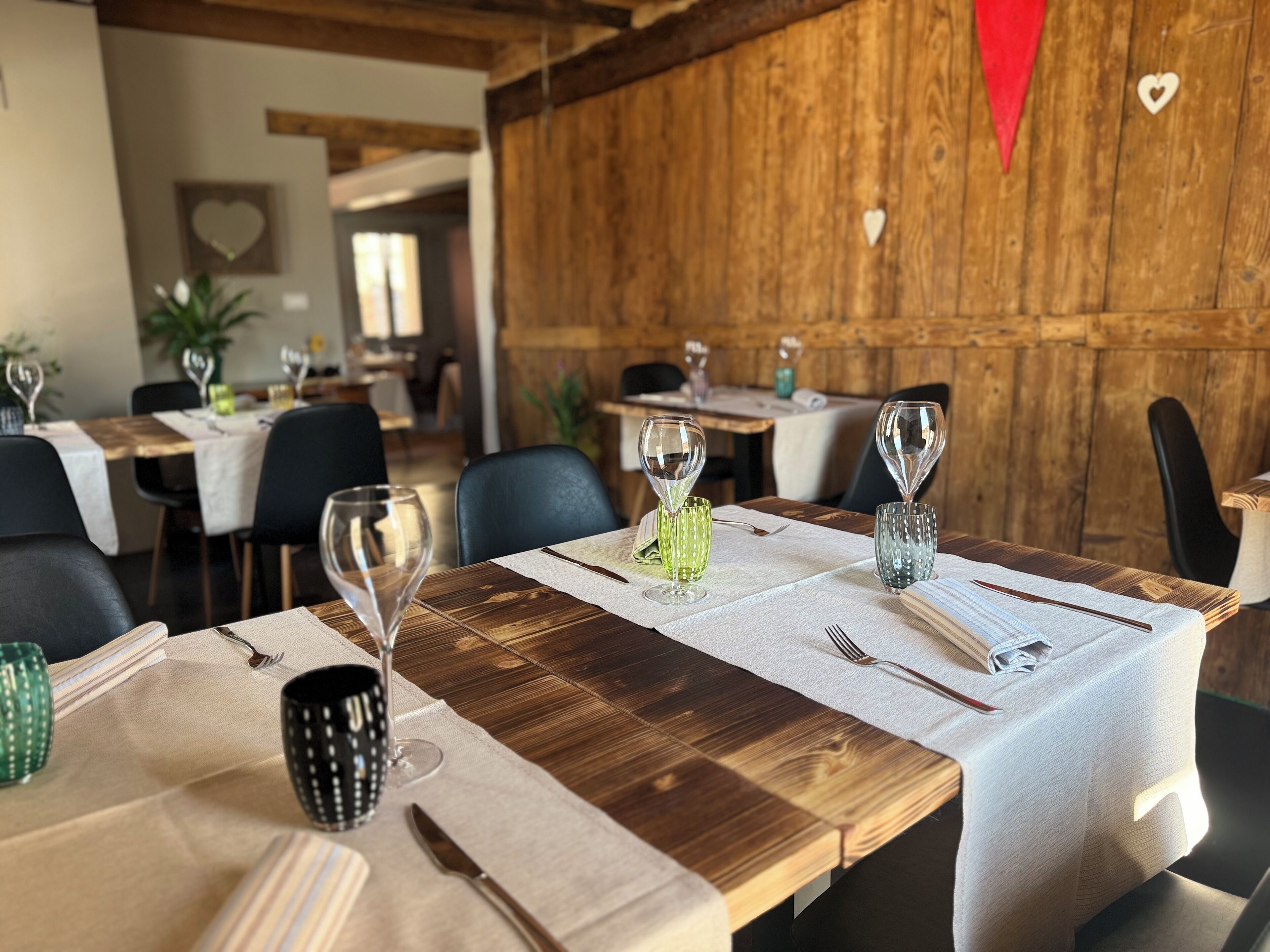 Un restaurante con mesas y sillas de madera, cada conjunto con una copa de vino, un florero verde y cubiertos.