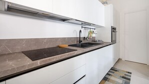 Una cocina moderna con armarios blancos, encimera de mármol, horno empotrado y campana extractora de acero inoxidable.
