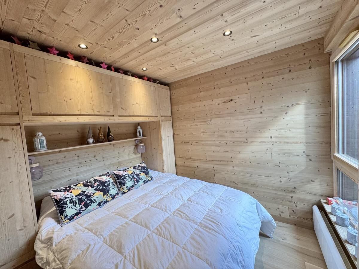 A wooden-paneled bedroom with a bed, shelves, and a window.