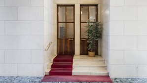 A building entrance with a red carpet leading to double doors, a potted plant, and a staircase. - Easylife - Cosmopolitan Style in Porta Venezia (Milano)