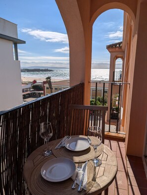 A balcony table set with plates, cutlery, and wine glasses, overlooking a beach and ocean. - 271- Livingtarifa Nomada (Tarifa)