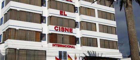 Un hotel de varios pisos con balcones, un estacionamiento y varias banderas.