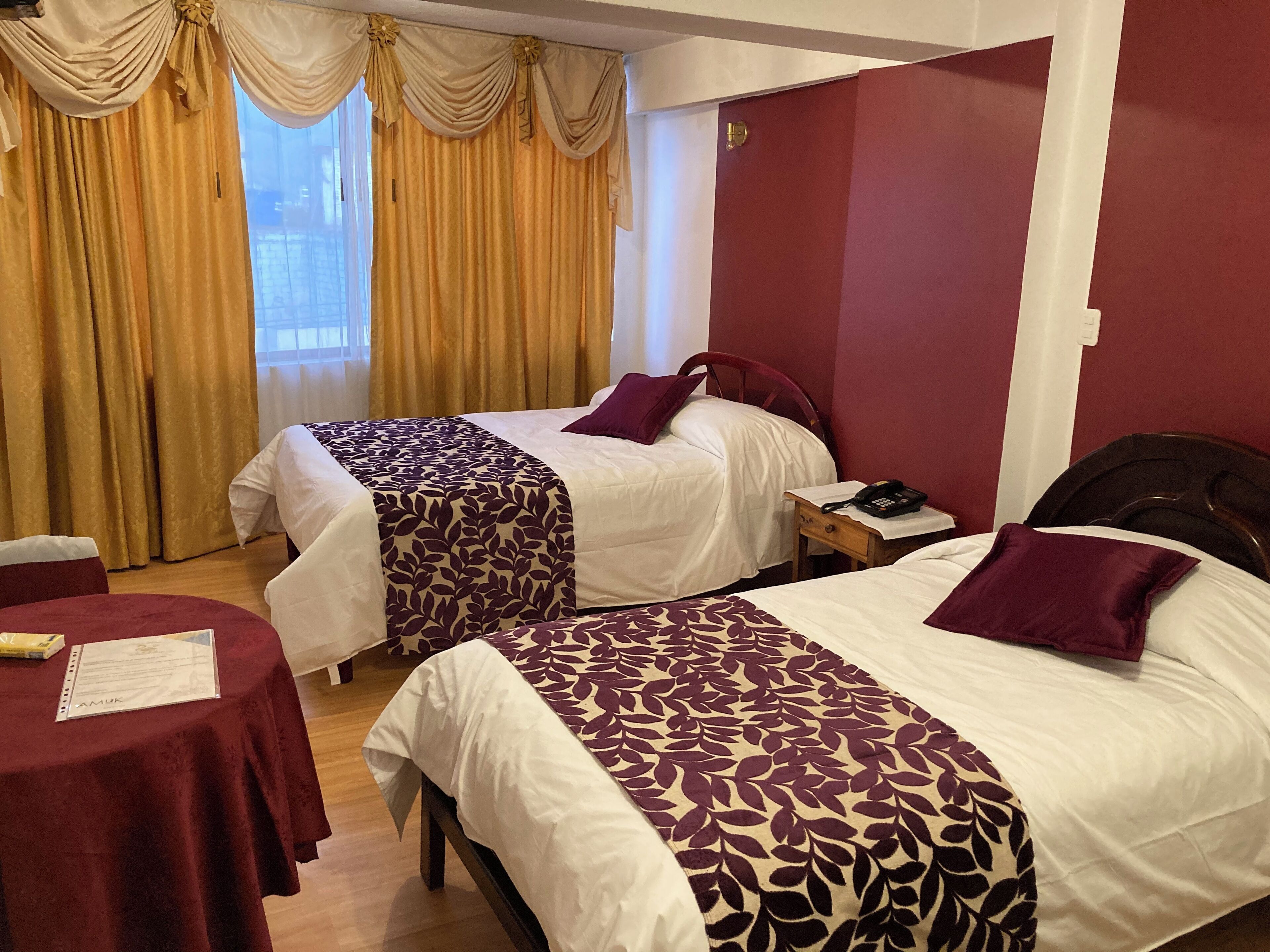 A hotel room with two beds, a small table, and a window with curtains.