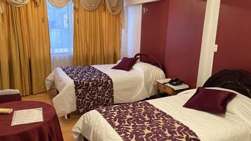 A hotel room with two beds, a small table, and a window with curtains.