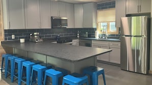 A modern kitchen with grey cabinets, a stainless steel refrigerator, and blue bar stools. - Camelback Cabin “Brand New” (Tannersville)
