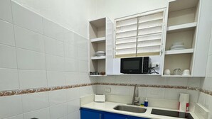 A compact kitchen with white tiled walls, a black refrigerator, blue cabinets, a microwave, and a sink.
