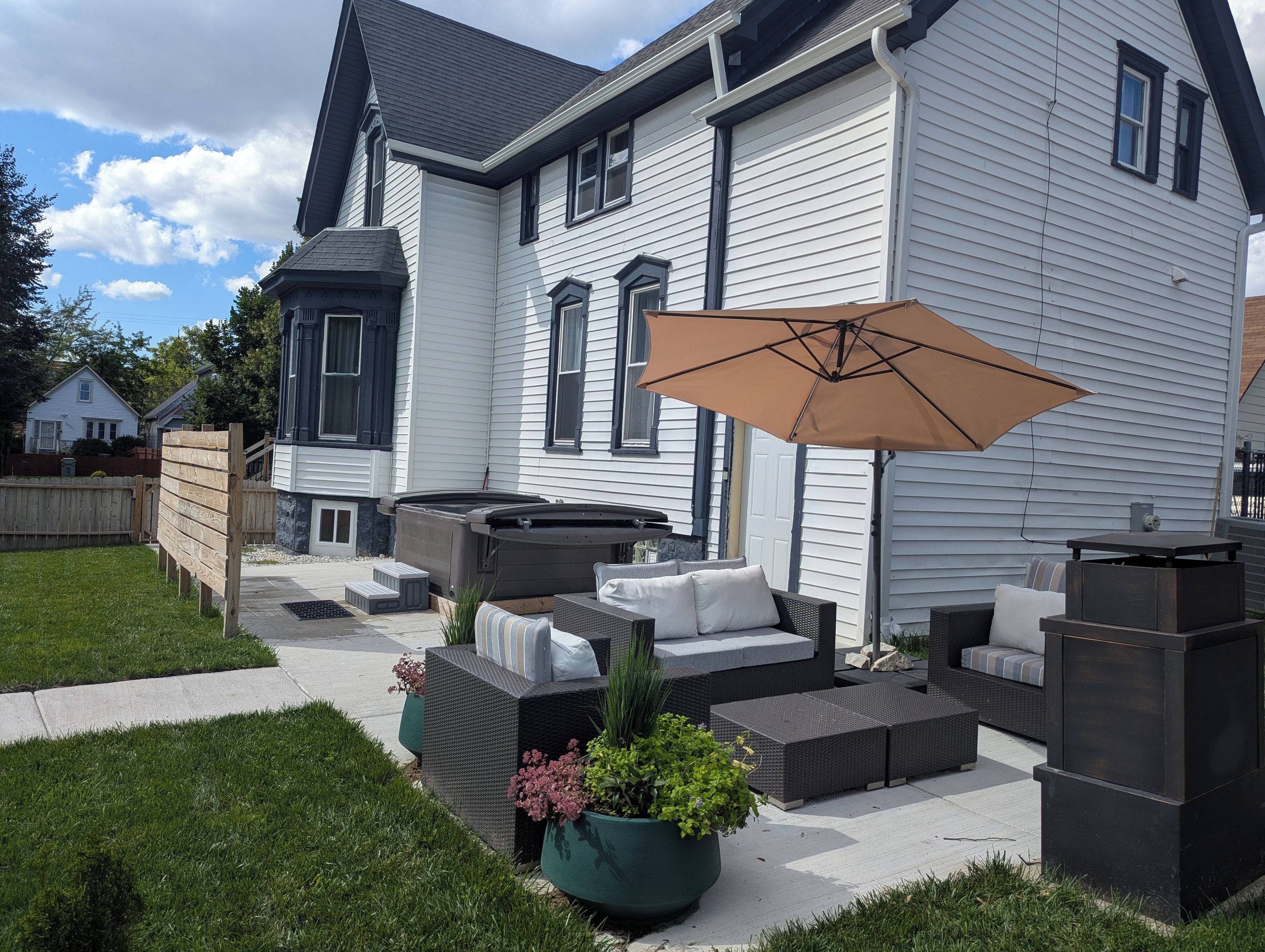 A residential property with a patio area featuring outdoor furniture, a hot tub, and a large umbrella.