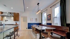 Una cocina moderna con armarios de madera, una isla central con taburetes de bar, una mesa de comedor con bancos y un ventanal con cortinas.