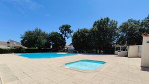 A swimming pool area with two pools, paved walkways, and surrounding trees. - Condominium with swimming pool and secure gated parking. (Saint palais sur mer)