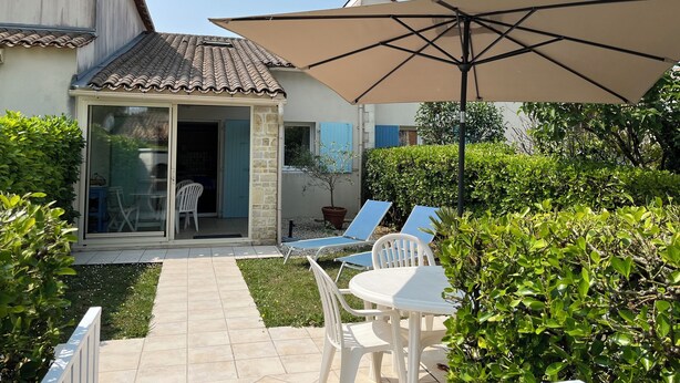 A patio area with a table and chairs, a large umbrella, and a small garden. - Condominium with swimming pool and secure gated parking. (Saint palais sur mer)