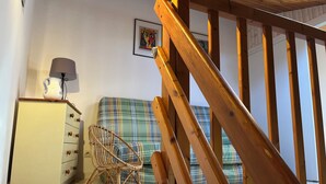 A wooden staircase leading to a room with a plaid sofa, a wicker chair, and a cream-colored cabinet with drawers. - Condominium with swimming pool and secure gated parking. (Saint palais sur mer)