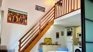 A kitchen with a microwave, oven, and washing machine. There is a wooden staircase with a railing. A table with chairs is visible. - Condominium with swimming pool and secure gated parking. (Saint palais sur mer)