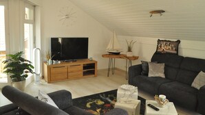 Sala de estar com televisão, sofá e uma pequena mesa com controle remoto.