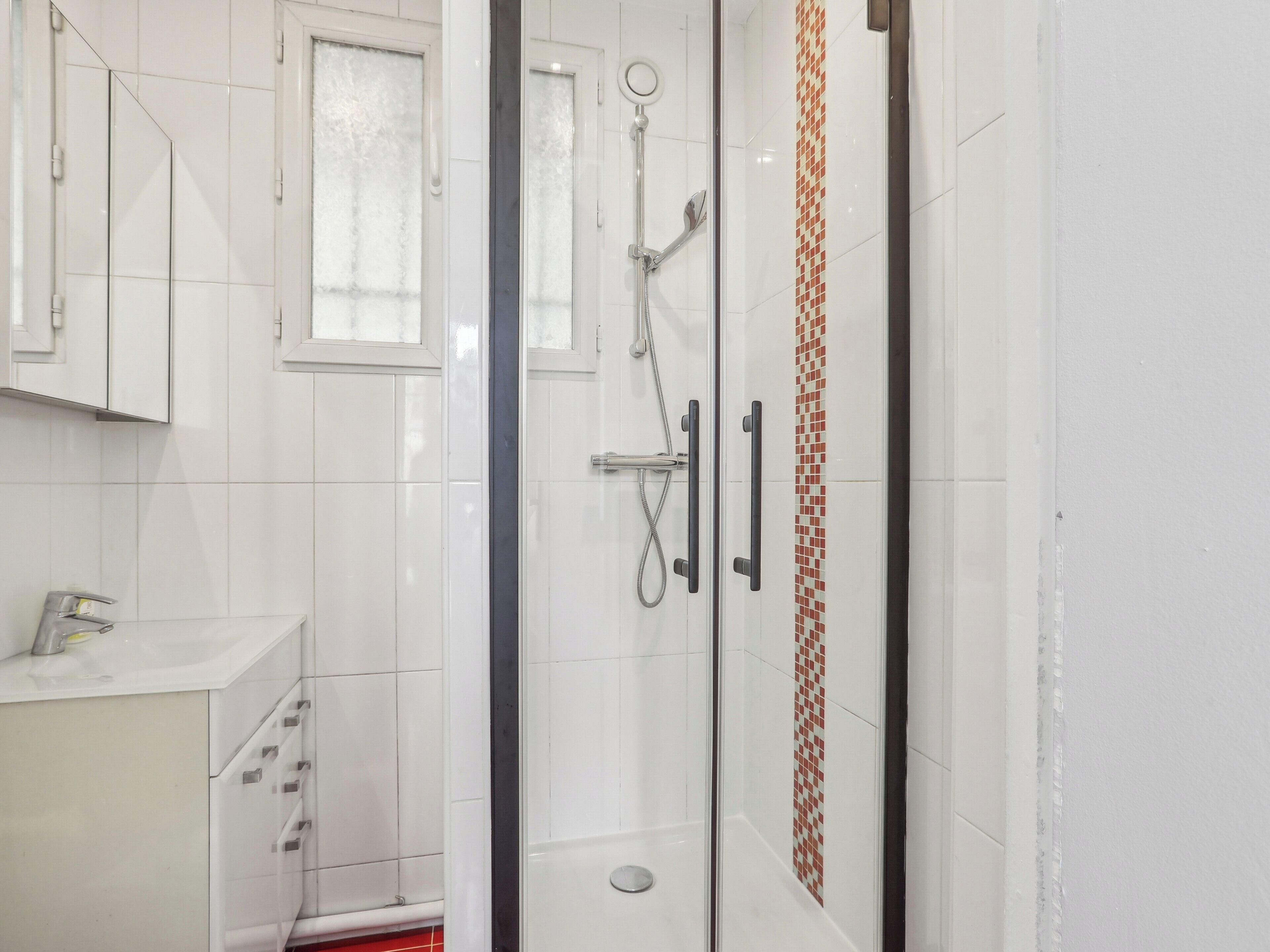 A modern bathroom with a glass shower enclosure, white tiled walls, and a small window.