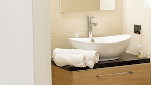 Un bagno moderno con un lavandino bianco, uno specchio sopra e un mobile bagno in legno con cassetti.