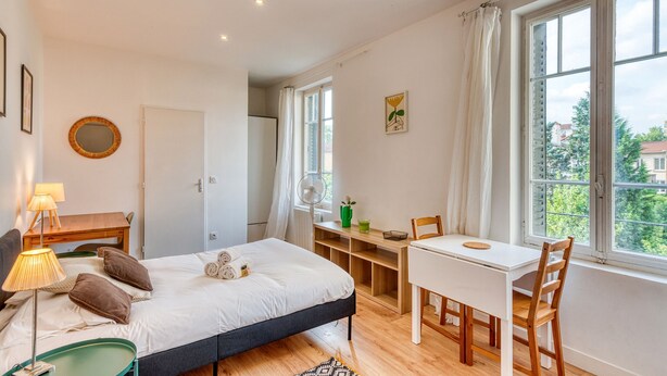 A bedroom with a bed, bedside table, lamp, and a desk with a chair.