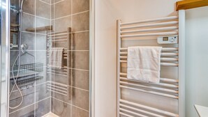A modern bathroom with a glass-enclosed shower, a white towel rack, and a digital thermostat.