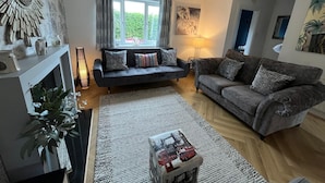 Ein Wohnzimmer mit einer Couch, einem Kamin, einem Teppich und einem Fenster mit Vorhängen.