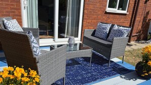 Ein Patio mit Korbmöbeln, einem Glastisch und einer blauen Matte.