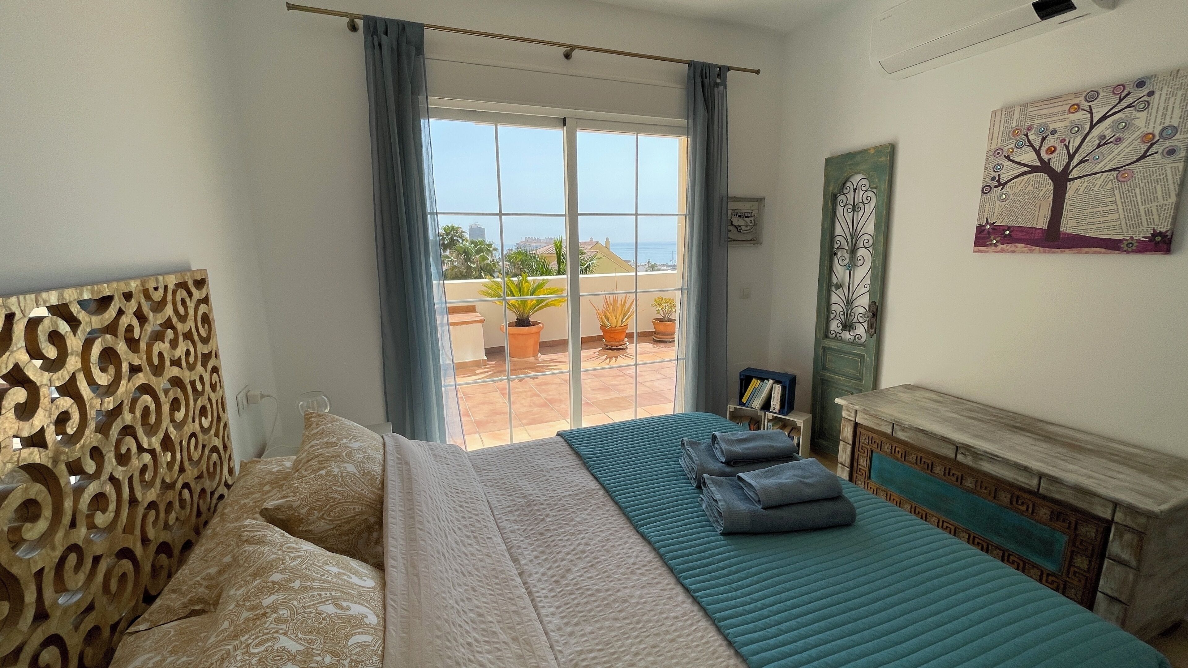 A bedroom with a bed, a view of the balcony, and a decorative wall piece.