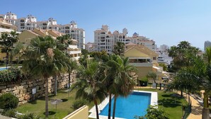 A resort with a swimming pool surrounded by palm trees and a stone wall. - Cozy one bedroom apartment with pool and garden views (Estepona)