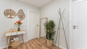 A hallway with a wooden floor, a white door, a mirror, a plant, and a decorative wall piece. - GuestReady - Lovely family home in Boavista (Boavista)
