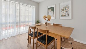 A dining area with a wooden table and chairs, a vase with flowers, and two framed artworks on the wall. - GuestReady - Lovely family home in Boavista (Boavista)
