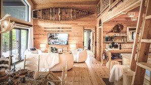 A spacious living area with a large TV, wooden furniture, and a dining table with chairs. - Hôtel à la maison - Villa le Pôle Nord (La Malbaie)
