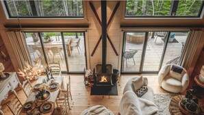 A cozy interior with a fireplace, wooden furniture, and large windows overlooking a deck. - Hôtel à la maison - Villa le Pôle Nord (La Malbaie)