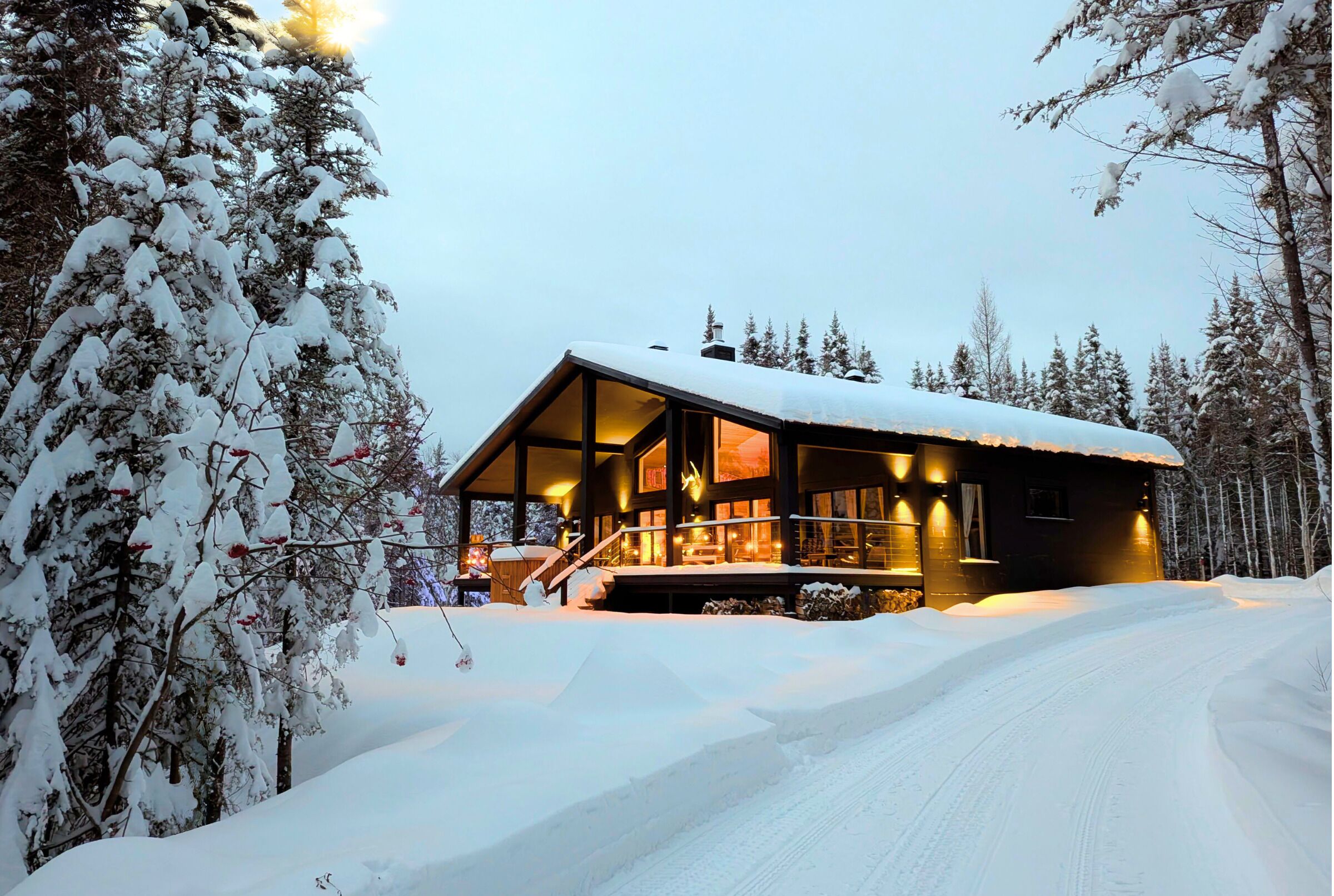 A snow-covered cabin with a wooden exterior, large windows, and a visible staircase leading to the entrance.