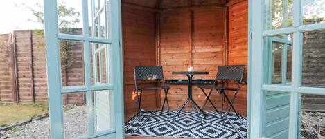 A wooden cabin with a small table and two chairs, a patterned rug on the floor, and a wooden fence in the background.