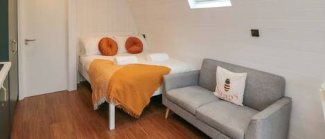 A cozy room with a bed, a grey sofa, and a skylight.