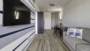 Ein modernes Wohnzimmer mit einem an der Wand befestigten Flachbildfernseher, einem grauen Sofa mit Zierkissen und einem Essbereich mit Tisch und Stühlen.