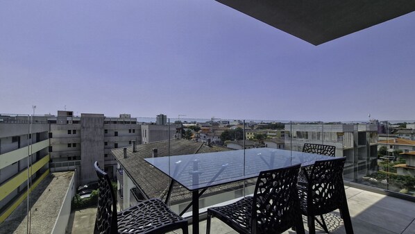 A rooftop terrace with a glass table and chairs, offering a view of surrounding buildings.