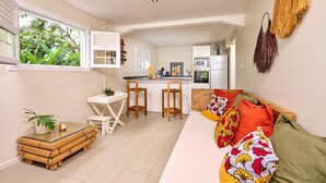A compact living space with a kitchen, dining area, and a sofa with colorful cushions. - Pymen - Cocon climatisé avec terrasse et jardin (Rivière-Salée)
