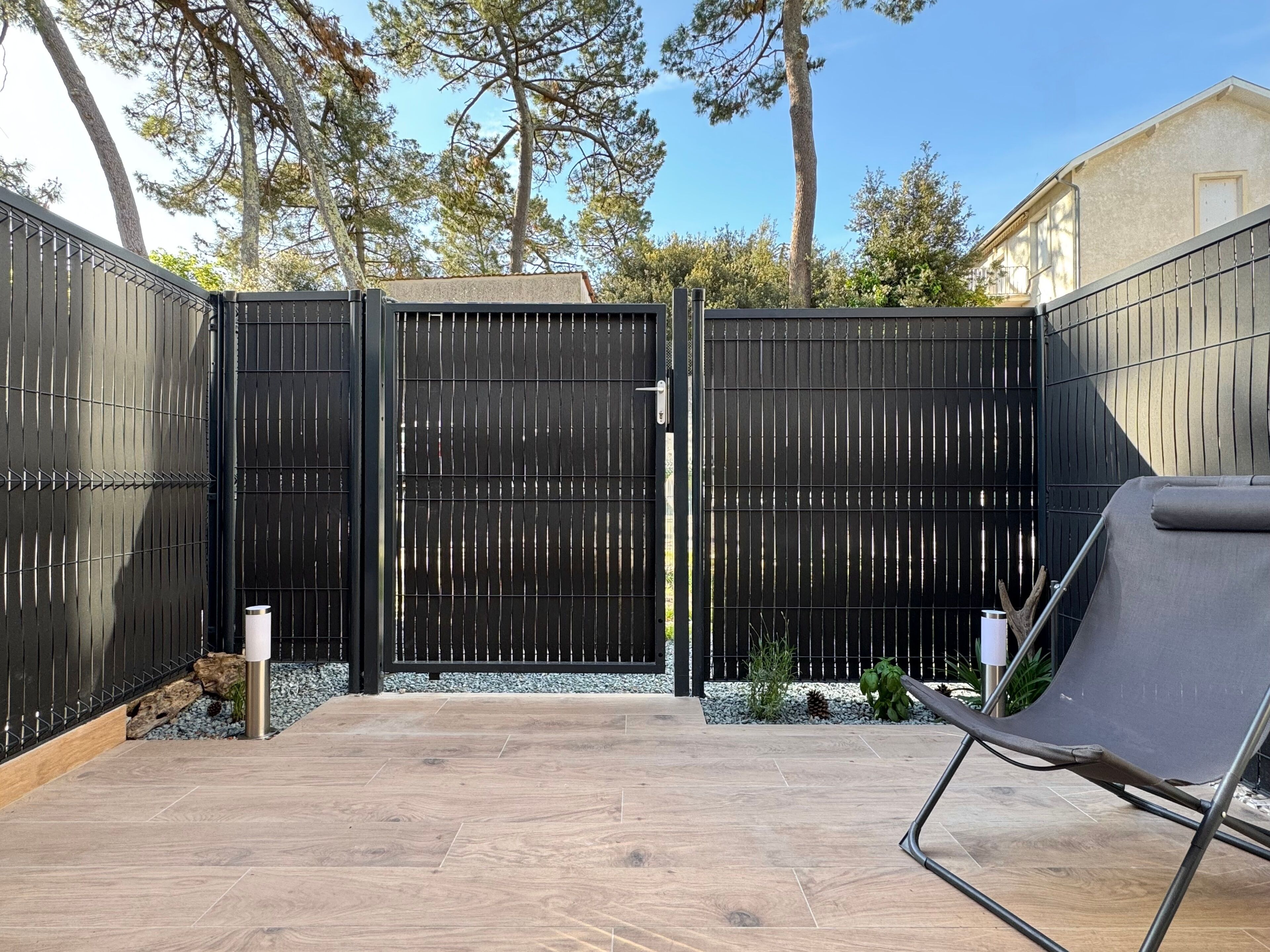 A patio with a black metal fence, a wooden deck, and a metal chair.