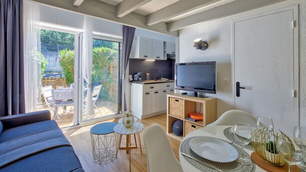 Una habitación moderna con sofá, mesa de comedor y televisor. Hay una zona de cocina con armarios y televisor.
