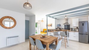 A modern kitchen with a dining area, featuring a wooden table and chairs, a round mirror, and a built-in oven.