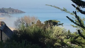 Vista costera con un edificio en primer plano, cielo despejado y una masa de tierra distante.