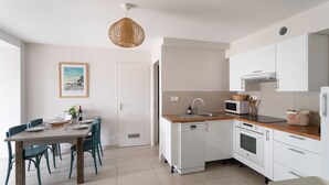 Una cocina moderna con armarios blancos, encimera de madera y lavavajillas. Hay una mesa de comedor con sillas y una lámpara colgante.