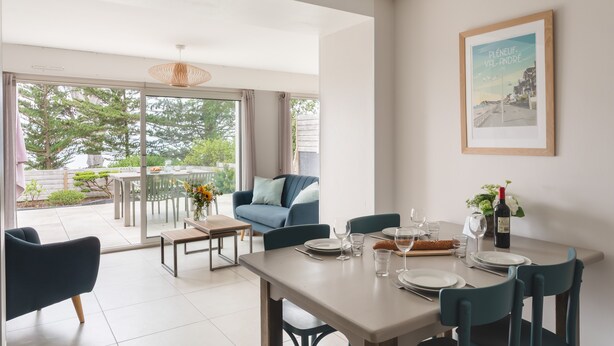 Un comedor con una mesa preparada para cuatro personas, un sofá y un ventanal con vistas a zonas verdes.