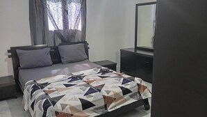 Une chambre à coucher avec un lit, une table de chevet, une commode et une fenêtre avec des rideaux.