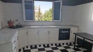 Une cuisine avec des meubles blancs, un carrelage noir et blanc, une fenêtre donnant sur des arbres et une cuisinière avec des casseroles.