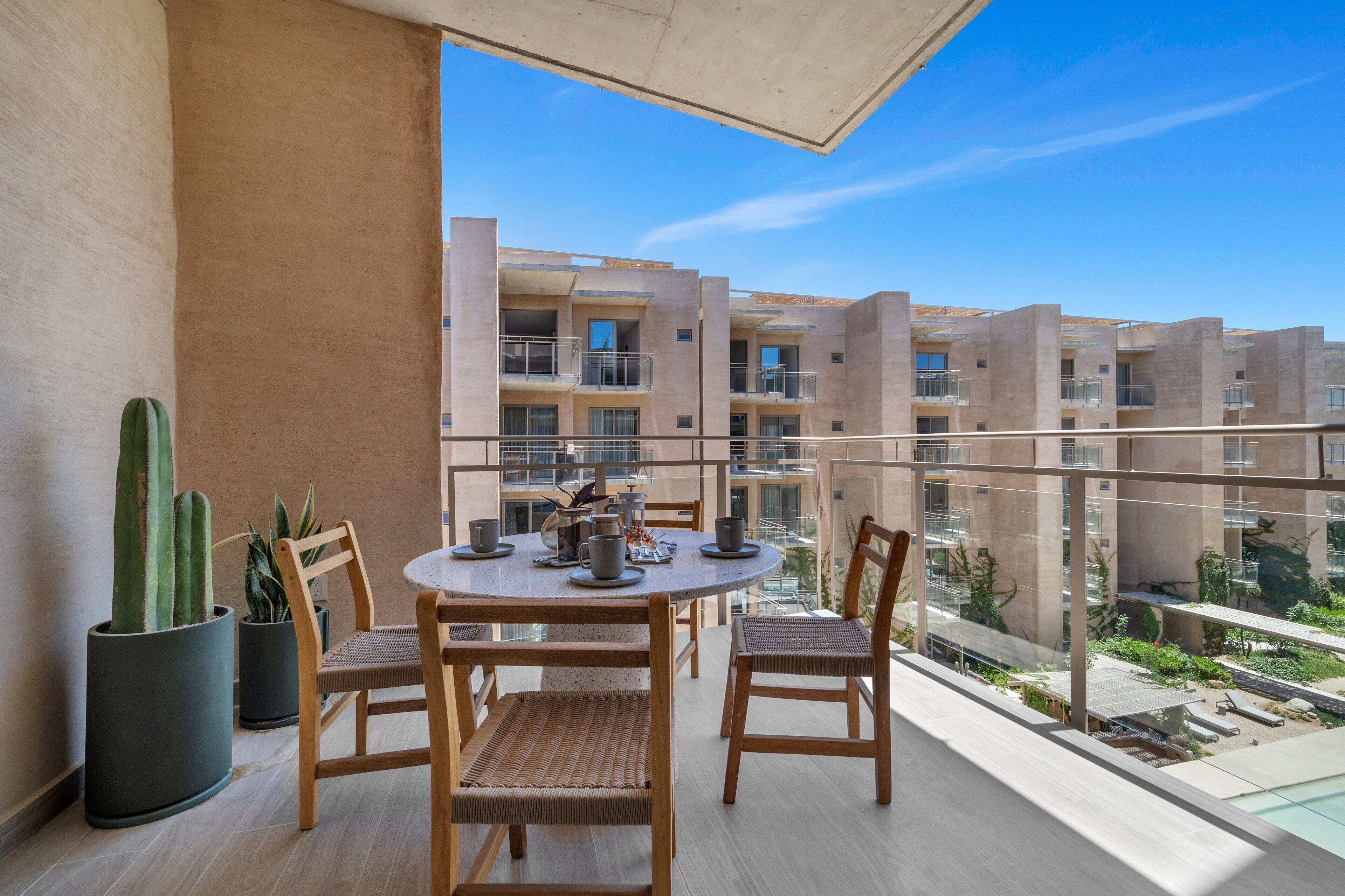 A balcony with a round table, chairs, potted plants, and a view of a building.