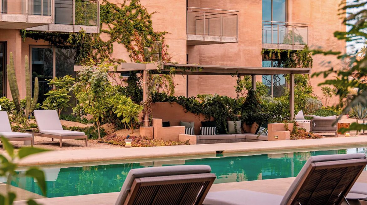 A poolside area with lounge chairs, a small seating area, and a building with a balcony.
