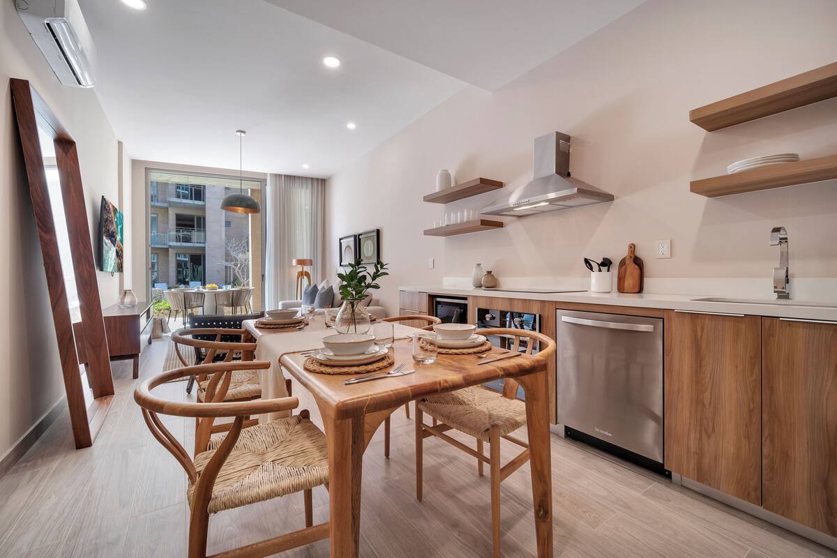 A modern kitchen with wooden cabinetry, a stainless steel dishwasher, and a dining area with a wooden table and chairs.