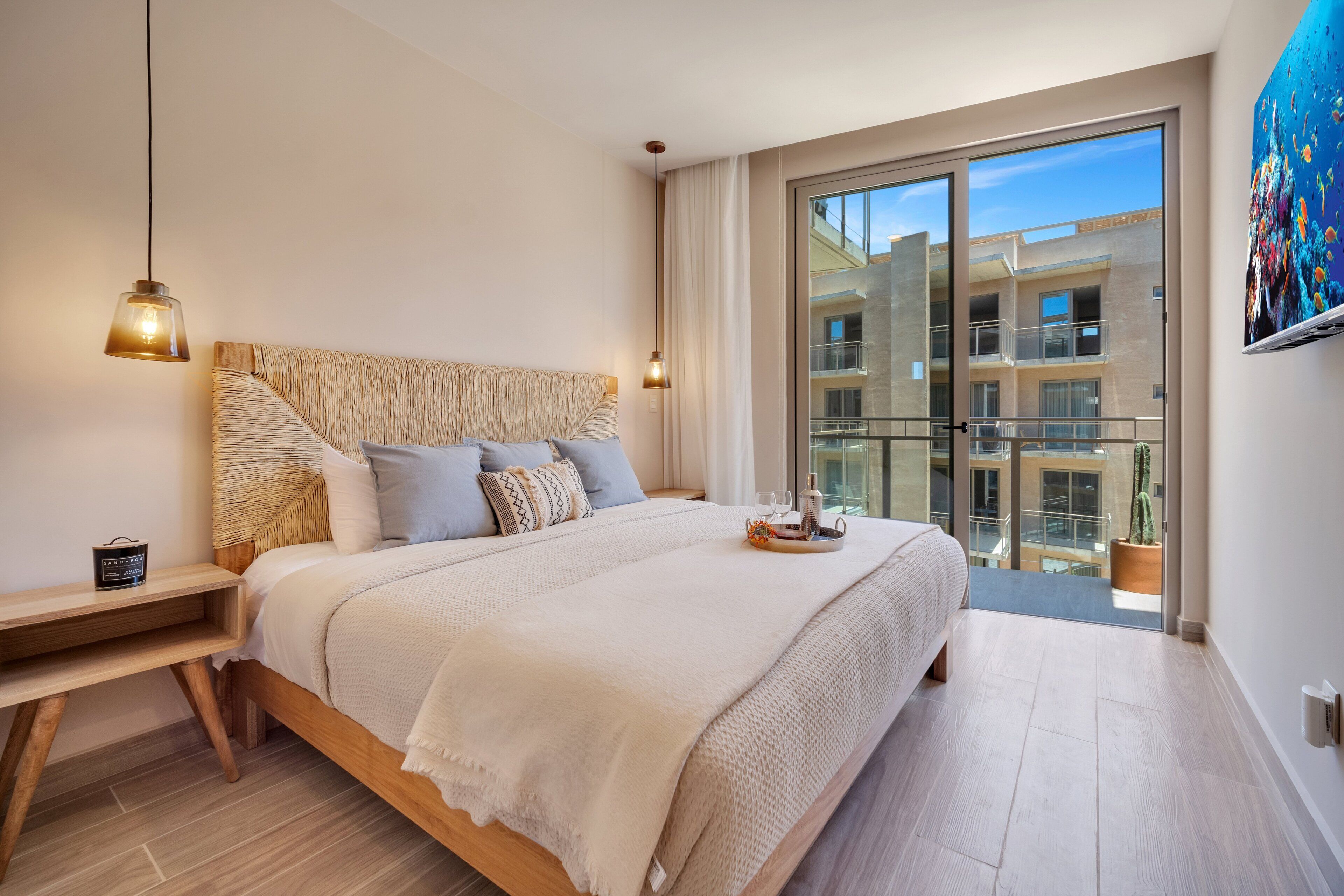 A modern bedroom with a large bed, bedside tables, a view of the balcony, and a painting on the wall.